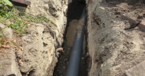 Exposed sewer pipe running through a trench, illustrating a sagging sewer line that can cause recurring backups.