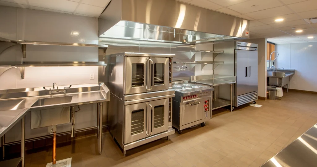 Stainless steel commercial kitchen with sinks, cooking equipment, refrigeration, and food preparation areas, illustrating common commercial kitchen plumbing systems and problems.
