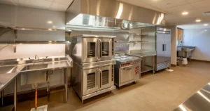 Stainless steel commercial kitchen with sinks, cooking equipment, refrigeration, and food preparation areas, illustrating common commercial kitchen plumbing systems and problems.