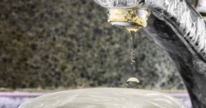 Close-up of a dripping faucet with mineral buildup, illustrating hard water plumbing problems and scale buildup.